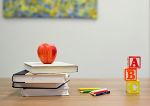 Stapel Bücher, Apfel und bunte Bauklötze auf Holztisch. Symbol für Bildung und Lernen.