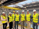 Personen in gelben Warnwesten und weißen Schutzhelmen in einer Industrieanlage.