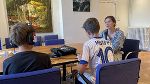 Gespräch zwischen drei Personen an einem Konferenztisch, eine Person hält dabei ein Mikrofon.