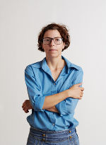 Die bildende Künstlerin Ulrike Königshofer zu sehen mit einer blauen Bluse und einer blauen Jean vor einem weißen Hintergrund.